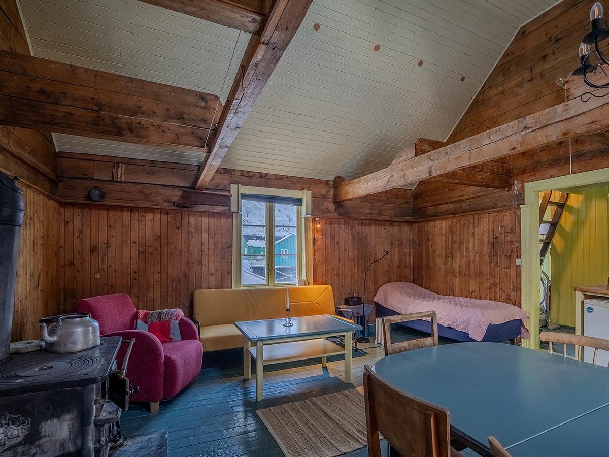 Cozy wooden cabin interior with seating, dining table and stove.