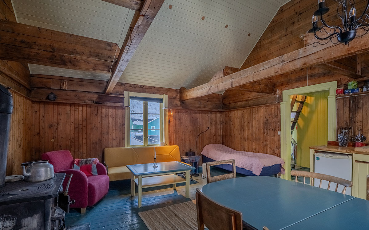 Cozy wooden cabin interior with seating, dining table and stove.