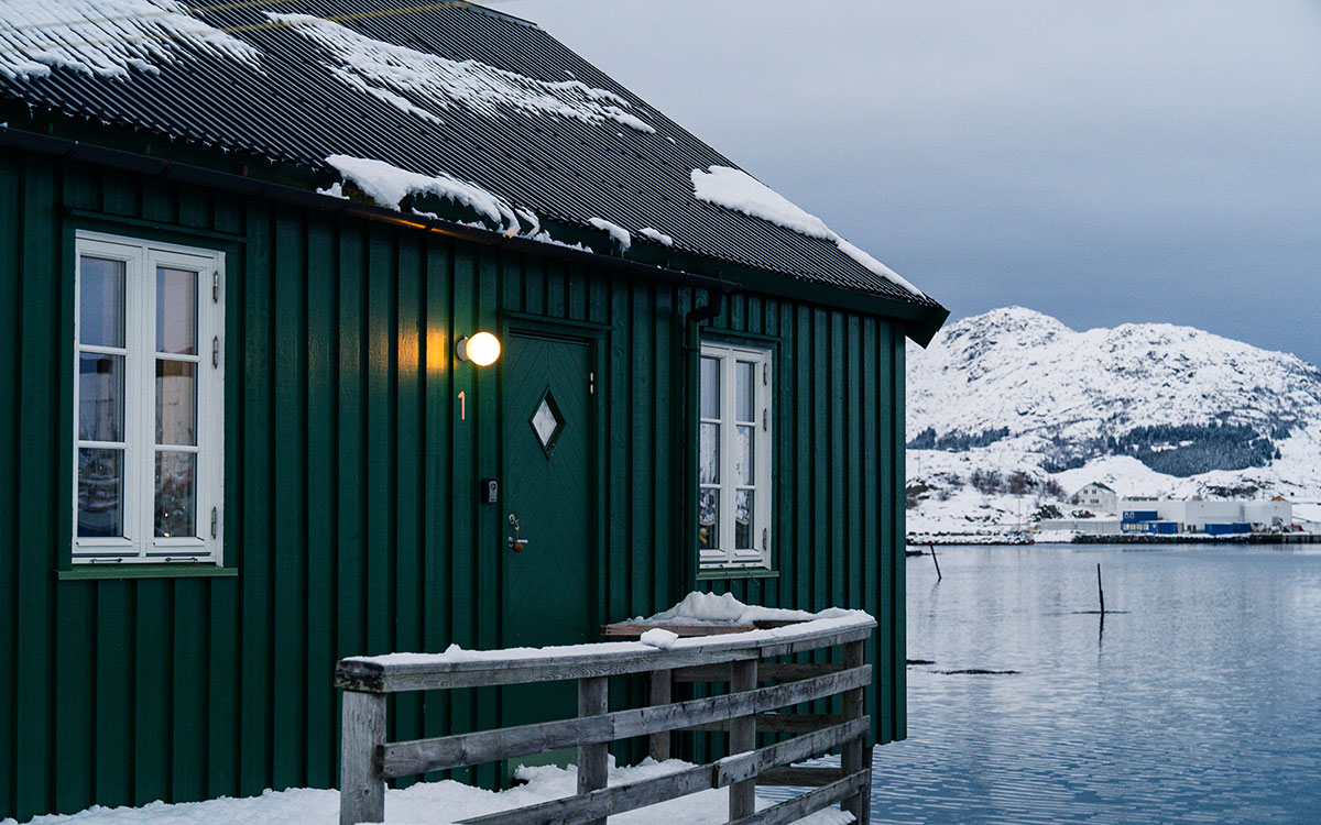 Green seaside cabin in snowy winter landscape, Lofoten.