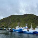 Fishing boats moored at the harbor in Ballstad with green mountain backdrop in the Lofoten Islands.