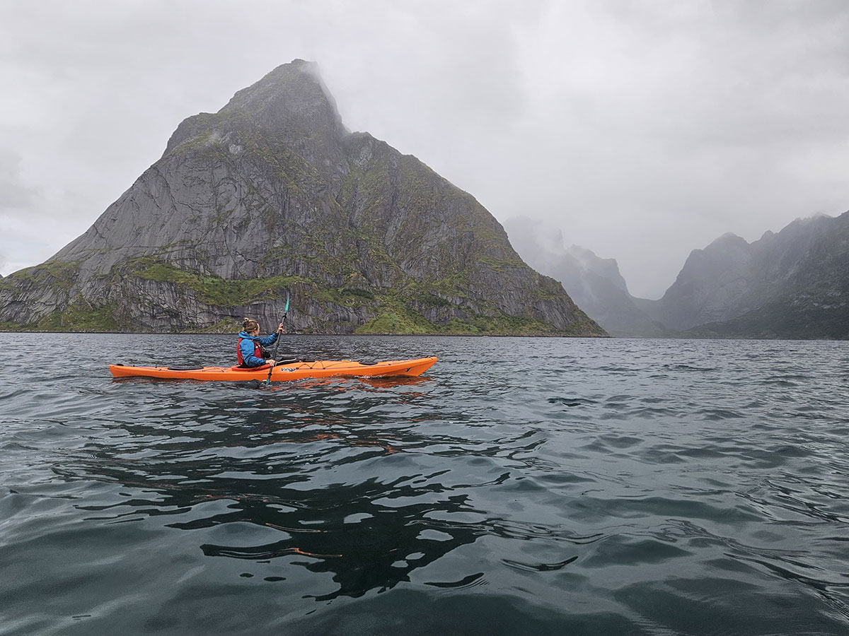 Kayaker on a fjord with steep mountains in Ballstad, Lofoten.